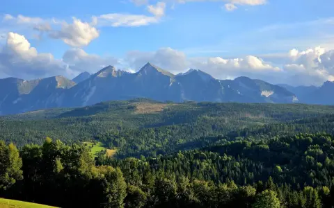 Widok na Tatry z przełęczy nad Łapszanką. Majestatyczne szczyty górskie, gęste lasy i błękitne niebo z chmurami.