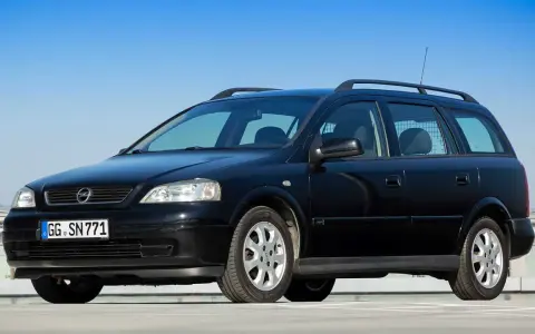 Schwarzer Opel Astra Kombi, alt, mit Dachreling und Kennzeichen GG SN 771, parkt auf einem Parkdeck vor blauem Himmel.