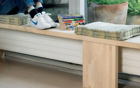 En person sitter på en bänk med kuddar och böcker. Under bänken finns ett element som är inbyggt i möbeln.