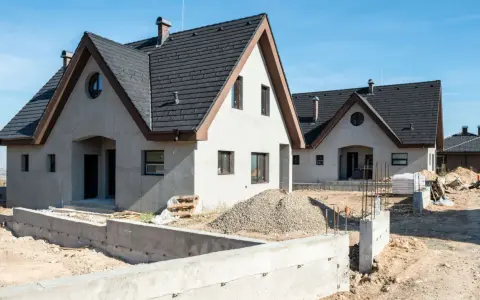 Nowe domy z betonu w budowie, z ciemnymi dachami i jasnymi ścianami, na tle błękitnego nieba.