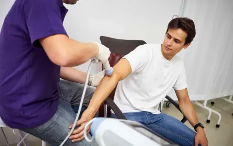 Fizjoterapeuta stosuje terapię falą uderzeniową na ramieniu pacjenta, aby złagodzić ból i przyspieszyć regenerację.