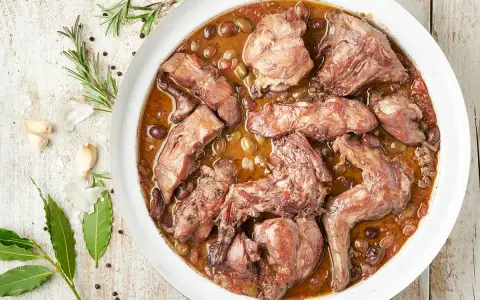 Coniglio in padella, un piatto succulento con olive e aromi, pronto per essere gustato.
