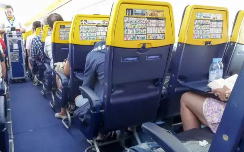 Wnętrze samolotu Boeing 737, rzędy miejsc dla pasażerów. Widok na siedzenia z żółtymi oparciami i instrukcjami bezpieczeństwa.