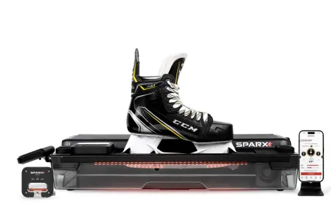 En hockeyklubba på en slipmaskin för slipning av skridskor. Bredvid syns en mobiltelefon med appen för slipning.