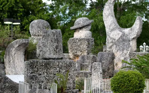 Sculture in pietra calcarea e corallo, tra cui un cappello e una forma a mezzaluna, creano un magico coral castle immerso nel verde.
