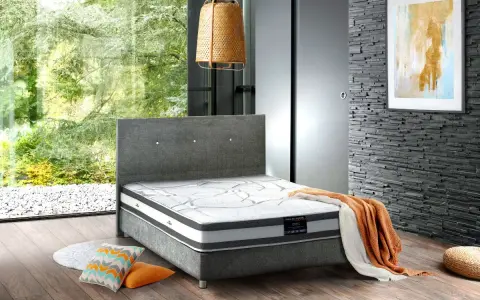 Un lit moderne avec un matelas de dimension queen size, des coussins colorés et une couverture orange sur un parquet en bois.