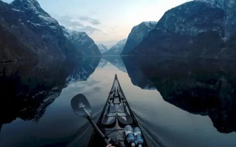 Kajakpaddling i en norsk fjord med snöklädda berg som speglar sig i det lugna vattnet. En fantastisk utsikt över son Norge.