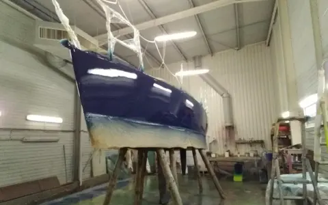 Un bateau bleu profond est en cours de stratification dans un atelier. La coque est soutenue par des tréteaux en bois.