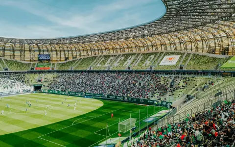 Widok na murawę i trybuny Polsat Plus Arena Gdańsk podczas meczu. Tłumy kibiców na zielonych krzesełkach.