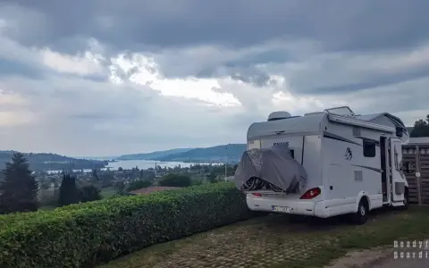 Kamper zaparkowany na kempingu w Czeskiej Szwajcarii, z widokiem na jezioro i wzgórza.