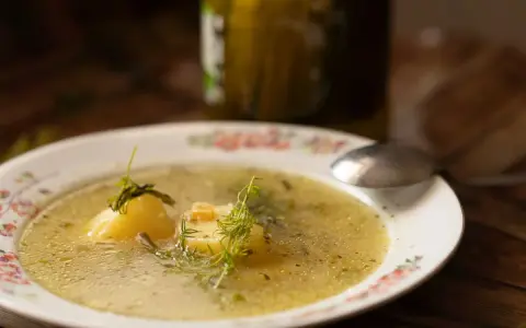 Aromatyczna keto zupa ogórkowa z ziemniakami i koperkiem, podana na talerzu z kwiatowym wzorem. Obok stoi słoik ogórków.