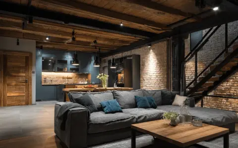 Un salon cosy avec un grand canapé gris, une cuisine moderne et un escalier industriel. Idéal pour aménager un souplex avec style.