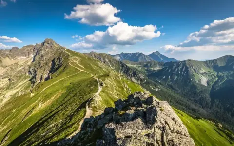 Widok na szlak prowadzący na Kasprowy Wierch. Zielone zbocza górskie, skaliste szczyty i błękitne niebo z chmurami.