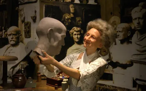 W muzeum figur woskowych artystka w historycznym stroju pracuje nad popiersiem.