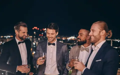 Eleganccy panowie w garniturach i muszkach, pijący drinki na tarasie. Idealny przykład, jak się ubrać na poprawiny.