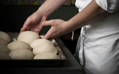 Mani esperte sistemano impasti per pizza, un mestiere che fa riflettere su quanto guadagna un pizzaiolo al mese.