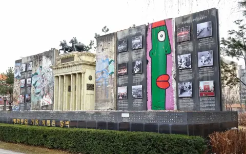 Fragment muru berlińskiego z graffiti i zdjęciami, obok replika Bramy Brandenburskiej.