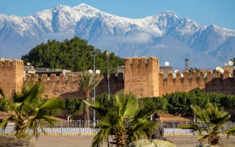 Marrakesz, gdzie leży, widać na tle ośnieżonych gór Atlas. Stare mury miasta i palmy tworzą malowniczy krajobraz.