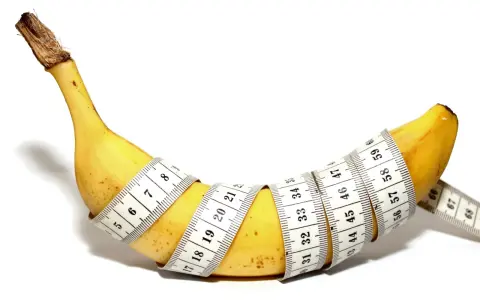 Żółty banan owinięty miarką krawiecką, pokazujący, jak wygląda penis.