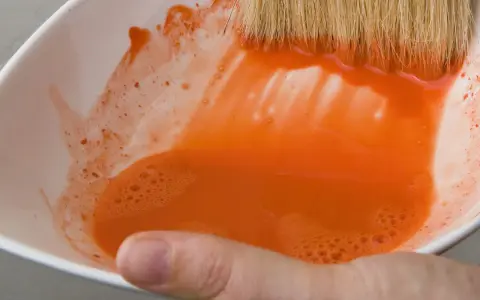 Maintenant, où jeter l'eau de rinçage des pinceaux ? Une main tient un bol blanc rempli d'eau orange trouble.