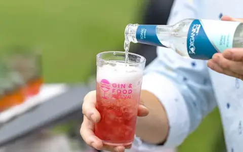 Tonic water wird in ein Glas mit rotem Getränk gegossen. Perfekt, um den Sommerdrink zu mischen.