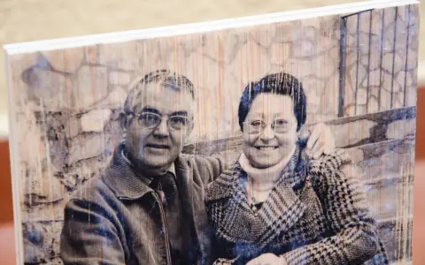 Pareja sonriente en un retrato transferir foto a madera, con un fondo de ladrillos y textura de madera visible.