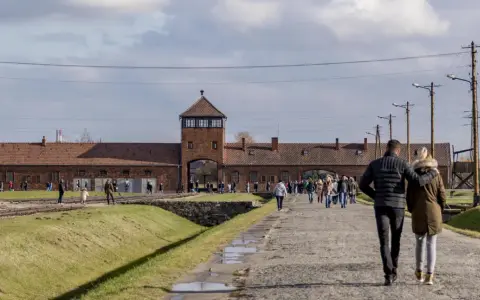 Spacer po terenie byłego obozu Auschwitz. Para idzie w stronę bramy z wieżą.