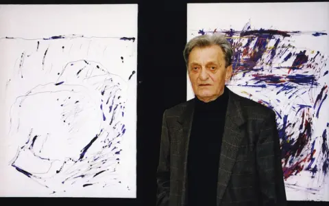Jacek Sempoliński, artysta, stoi obok swoich abstrakcyjnych obrazów.