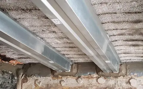 Vigas metálicas instaladas para como reforzar una viga de madera dañada por el fuego. Se observa el soporte de las nuevas vigas sobre la estructura existente.