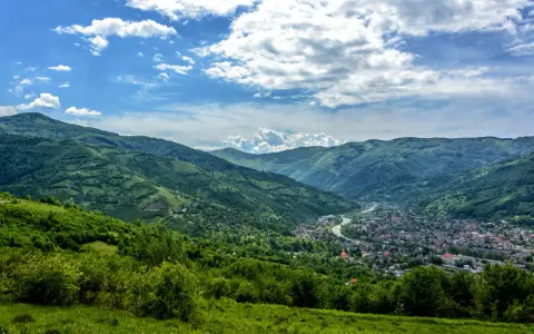 Zielone wzgórza Karpat na Ukrainie, z miasteczkiem w dolinie i rzeką.