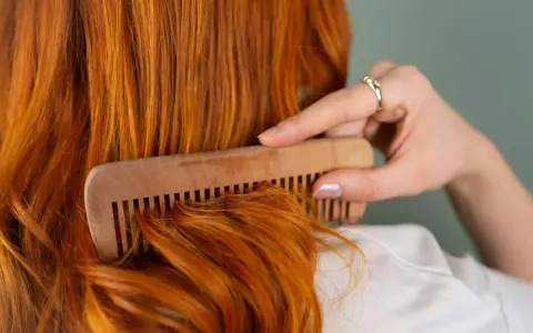 Mujer peina su cabello pelirrojo con un peine de madera. ¿En qué época del año se cae más el pelo? El otoño es conocido por ser el momento en que el cabello se cae más.