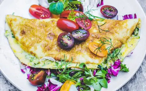Złocisty omlet z cukinią, podany z kolorową sałatką i pomidorkami koktajlowymi. Pyszne i zdrowe śniadanie.