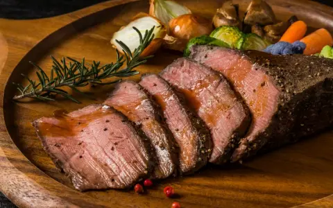 Succulento arrosto di manzo affettato, servito su un tagliere di legno con verdure arrosto, cipolle e rosmarino.