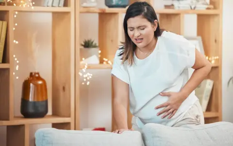 Frau mit schmerzverzerrtem Gesicht hält ihren Bauch, als ob sie Wehen erkennen würde.