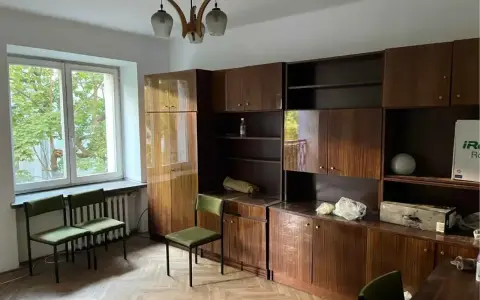 Pokój z meblościanką, oknem i krzesłami. Idealne miejsce na flipowanie mieszkania, by nadać mu nowy blask.