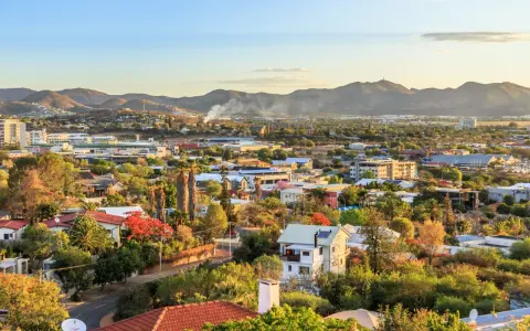 Widok na miasto Windhoek w Namibii o zachodzie słońca. W oddali góry, a bliżej zabudowania mieszkalne i komercyjne, otoczone bujną zielenią.