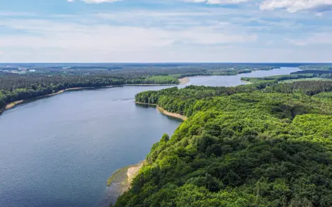 Malownicze jezioro otoczone lasem, idealne miejsce na nietypowe atrakcje Mazury. Widok z lotu ptaka na spokojną taflę wody i bujną zieleń.