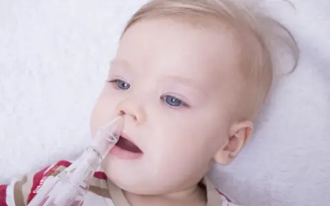 Niemowlę z niebieskimi oczami i blond włosami, któremu odciąga się katar za pomocą aspiratora.