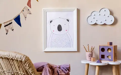 Adorable cuadros infantiles de un koala y una nube decoran la pared de una habitación. Una guirnalda de banderines alegra el ambiente.