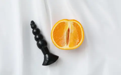 Czarny dildo obok przekrojonej pomarańczy, sugerujący orgazm analny.