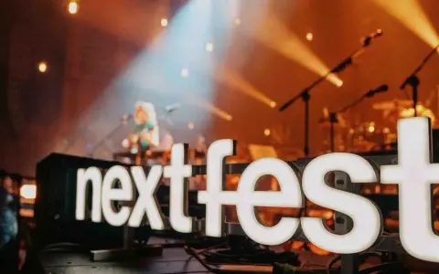 Światła sceny oświetlają napis "next fest" i artystkę grającą na gitarze.