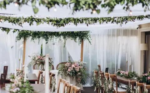 Uroczyste stoły i krzesła ozdobione zielenią i kwiatami tworzą magiczną atmosferę. Idealne na styl boho wesele.