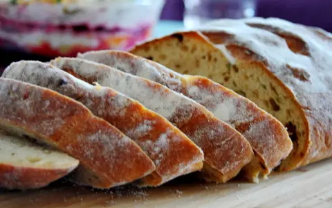 Pokrojony chleb z pomidorami, posypany mąką, leży na desce. W tle widać sałatkę.