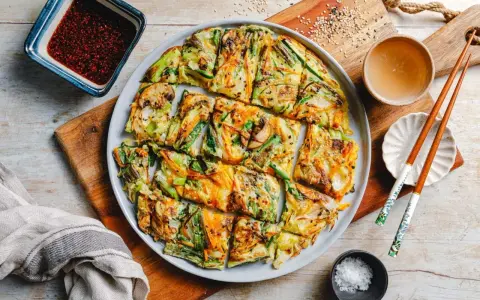 Bunte koreanische Pfannkuchen mit Gemüse, Pilzen und Karotten, serviert mit Dip und Stäbchen.