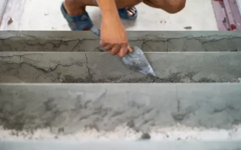 Ręka z kielnią wyrównuje betonowe schody wewnętrzne. To dobry sposób, czym wyrównać schody betonowe wewnętrzne.