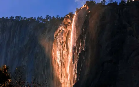 La luz del atardecer ilumina una cascada de fuego en un acantilado rocoso, creando un espectáculo natural.