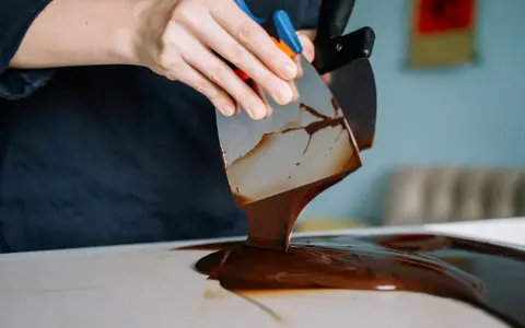 Mains travaillant du chocolat brillant sans tempérage avec des spatules. La texture fondante et lustrée promet une gourmandise parfaite.