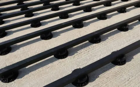 Rows of black synthetic lumber are elevated on black adjustable pedestals, creating a modern deck base on a concrete surface.