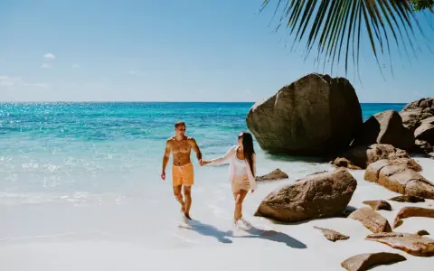 Para na Seszelach cieszy się idealną pogodą, spacerując po plaży z turkusową wodą i skałami.