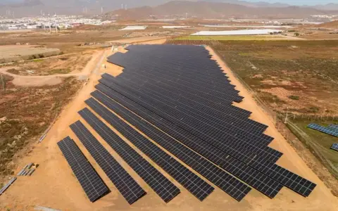 Große Solaranlage in Spanien, die die "Sonnensteuer" umgeht und saubere Energie liefert. Im Hintergrund Windräder und eine Stadt.